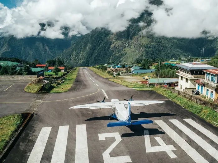 Một chiếc máy bay chuẩn bị cất cánh từ đường băng 24 tại Sân bay Tenzing-Hillary ở Nepal với nền là mây, núi và cây xanh.