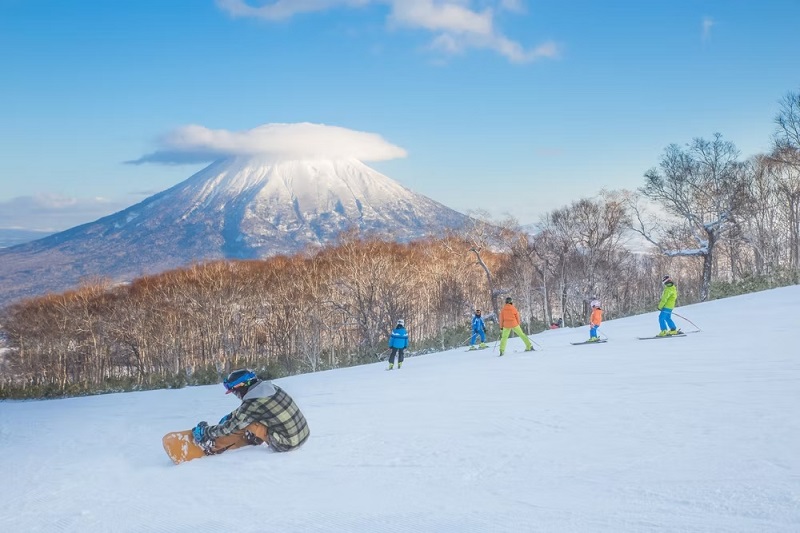 Mọi người trượt tuyết trên sườn núi tuyết với Núi Yotei gần đó ở khu trượt tuyết Niseko, Hokkaido, Nhật Bản