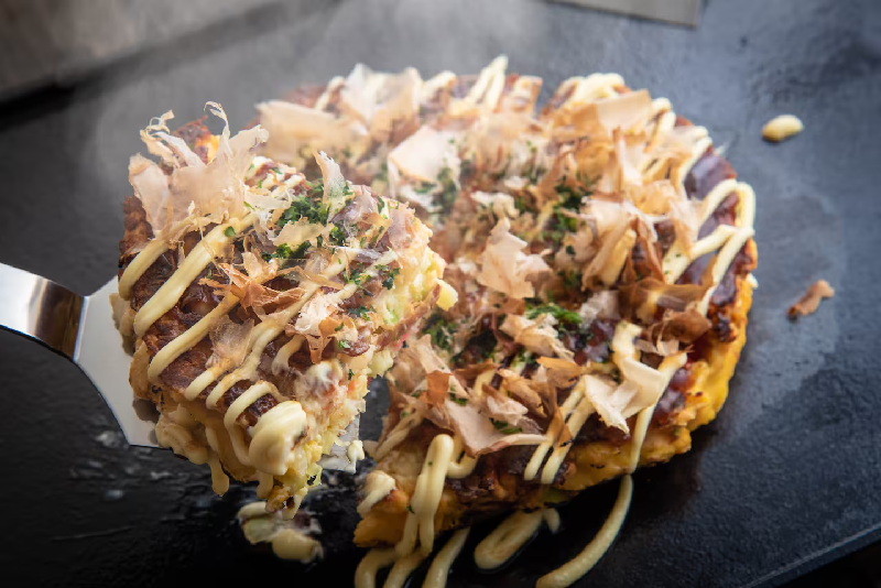 Okonomiyaki, một loại bánh xèo mặn, là món ăn đặc trưng ở Osaka, thường được nấu trên đĩa nóng chung. Ảnh / 123rf